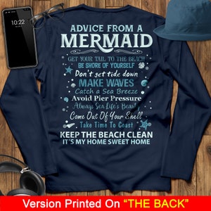 May include: A navy blue long-sleeved t-shirt with white text that reads "Advice from a Mermaid" and includes a list of tips for enjoying the beach. The text includes phrases like "Get your tail to the beach", "Be shore of yourself", "Don't get tide down", "Make waves", "Catch a sea breeze", "Avoid pier pressure", "Always sea life's beauty", "Come out of your shell", "Take time to coast", "Keep the beach clean", and "It's my home sweet home".