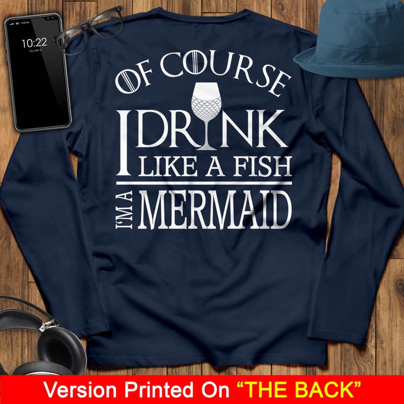 May include: A navy blue long-sleeved shirt with white text that reads "Of course I drink like a fish, I'm a mermaid". The text is centered on the back of the shirt and includes a graphic of a wine glass with a mermaid tail.