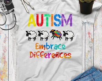 May include: White t-shirt with the word "AUTISM" in rainbow colors and a line of four sheep, one with a puzzle piece on its back. The text "Embrace Differences" is below the sheep in rainbow colors.