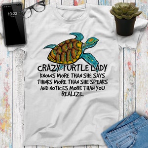 May include: White t-shirt with a colorful mandala-style turtle design and the text "Crazy Turtle Lady Knows More Than She Says Thinks More Than She Speaks And Notices More Than You Realize."