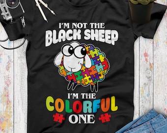 May include: Black t-shirt with a white sheep with a colorful puzzle piece design. The text "I'm not the black sheep I'm the colorful one" is printed on the shirt.