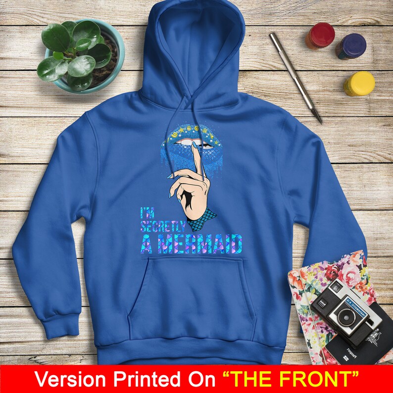 Peut inclure: Sweat-shirt &agrave; capuche bleu avec un graphique de l&egrave;vres bleues et violettes avec un doigt dessus, et le texte "I'm Secretly A Mermaid".
