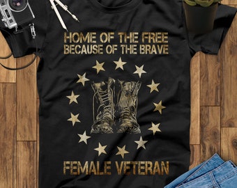Puede incluir: Camiseta negra con un estampado dorado de un par de botas militares y estrellas. El texto "Home of the Free Because of the Brave" y "Female Veteran" está impreso en la camiseta.