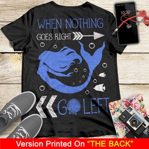 May include: Black t-shirt with a white mermaid design and the text "When nothing goes right, go left". The mermaid is blue and has a white seashell in her tail. The text is written in a handwritten style.