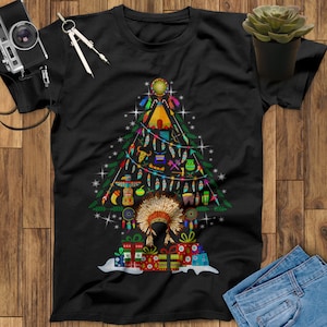 May include: Black t-shirt with a Native American Christmas tree design. The tree is decorated with traditional Native American symbols and ornaments, including feathers, dreamcatchers, and a headdress. The tree is topped with a star and surrounded by presents.