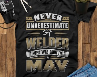 May include: Black t-shirt with gold text that reads "Never underestimate a welder who was born in May".