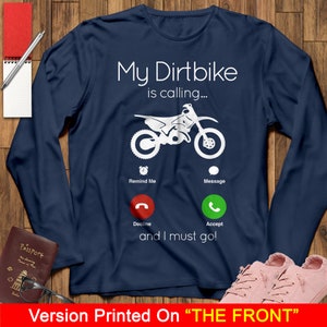 May include: A navy blue long-sleeved t-shirt with a white graphic of a dirt bike with a phone screen showing a missed call. The text on the shirt reads "My Dirtbike is calling... Remind Me, Message, Decline, Accept, and I must go!"