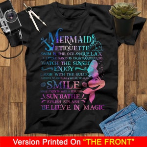 May include: A black t-shirt with a mermaid graphic and text that reads "Mermaid Etiquette: Swim in the ocean relax, a little sand is okay, watch the sunset, enjoy, laugh with the gulls, gather seashells wear pearls, smile, make friends with a starfish, sun bathe, splish splash, believe in magic".