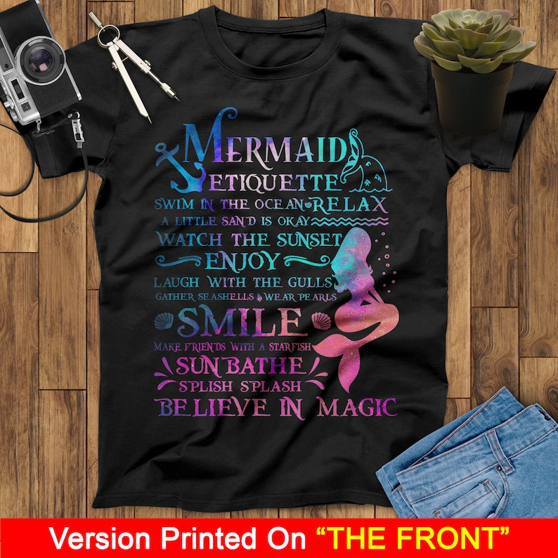 May include: A black t-shirt with a mermaid graphic and text that reads "Mermaid Etiquette: Swim in the ocean relax, a little sand is okay, watch the sunset, enjoy, laugh with the gulls, gather seashells wear pearls, smile, make friends with a starfish, sun bathe, splish splash, believe in magic".