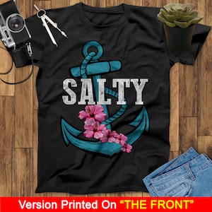 May include: A black t-shirt with a blue anchor and pink flowers. The text "SALTY" is printed in white above the anchor.
