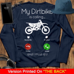 May include: A navy blue long-sleeved t-shirt with a white graphic of a dirt bike and a phone screen with the text "My Dirtbike is calling... Remind Me Message Decline Accept and I must go!" printed on the back.