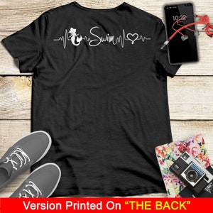 Puede incluir: Camiseta negra con una sirena blanca, un coraz&oacute;n y la palabra "Swim" en un gr&aacute;fico de latido del coraz&oacute;n. El gr&aacute;fico est&aacute; impreso en la parte posterior de la camiseta.