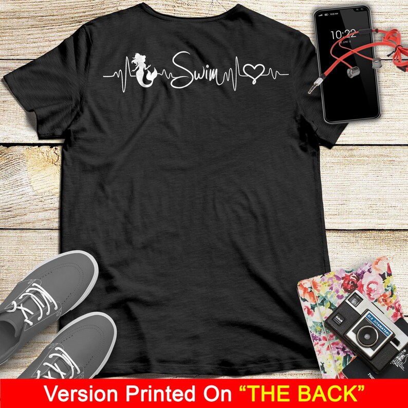 Puede incluir: Camiseta negra con una sirena blanca, un coraz&oacute;n y la palabra "Swim" en un gr&aacute;fico de latido del coraz&oacute;n. El gr&aacute;fico est&aacute; impreso en la parte posterior de la camiseta.