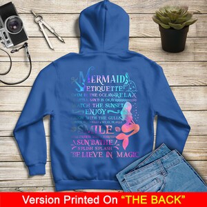 May include: A blue hoodie with a mermaid design and the text "Mermaid Etiquette" with a list of mermaid rules. The text is in a rainbow gradient.