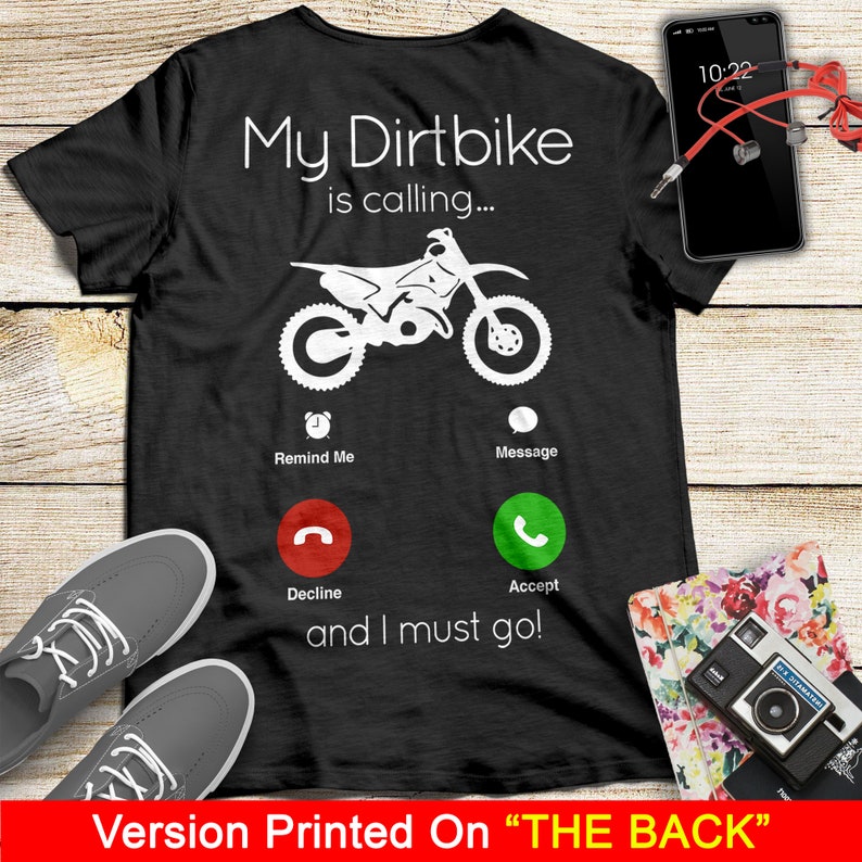 May include: Black t-shirt with a white graphic of a dirt bike with the text "My Dirtbike is calling..." and a phone icon with the options "Remind Me", "Message", "Decline", and "Accept". The text "and I must go!" is below the phone icon.