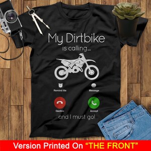 May include: Black t-shirt with a white graphic of a dirt bike with the text "My Dirtbike is calling..." and a phone icon with the options "Remind Me", "Message", "Decline", and "Accept". The text "and I must go!" is below the phone icon.