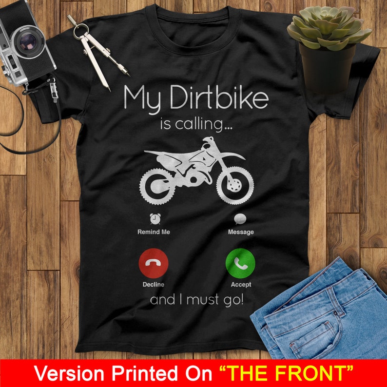 May include: Black t-shirt with a white graphic of a dirt bike with the text "My Dirtbike is calling..." and a phone icon with the options "Remind Me", "Message", "Decline", and "Accept". The text "and I must go!" is below the phone icon.