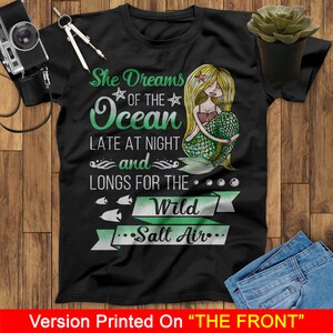 May include: Black t-shirt with a green mermaid illustration and the text "She Dreams of the Ocean Late at Night and Longs for the Wild Salt Air."