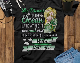 May include: Black t-shirt with a green mermaid illustration and the text "She Dreams of the Ocean Late at Night and Longs for the Wild Salt Air."