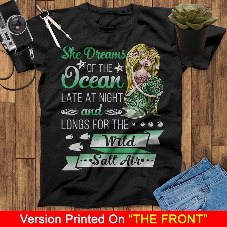 May include: Black t-shirt with a green mermaid illustration and the text "She Dreams of the Ocean Late at Night and Longs for the Wild Salt Air."