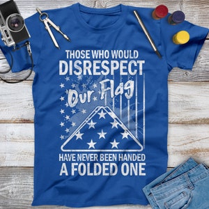 May include: A blue t-shirt with a white distressed graphic that reads "Those who would disrespect our flag have never been handed a folded one". The graphic includes a folded American flag with stars.