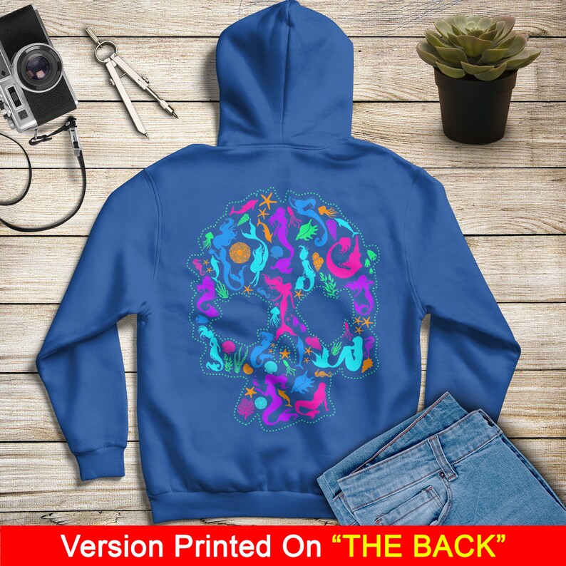 May include: A royal blue hoodie with a skull design made up of colorful mermaids, seashells, and starfish. The design is printed on the back of the hoodie. "Version Printed On "THE BACK"" is printed at the bottom of the image.