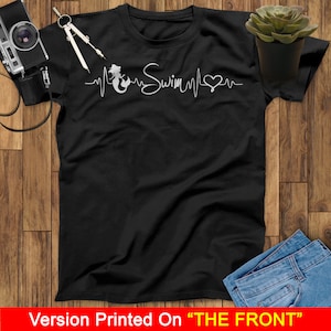 Puede incluir: Camiseta negra con un gr&aacute;fico blanco de una sirena con una l&iacute;nea de latido del coraz&oacute;n y la palabra "Swim" en cursiva.