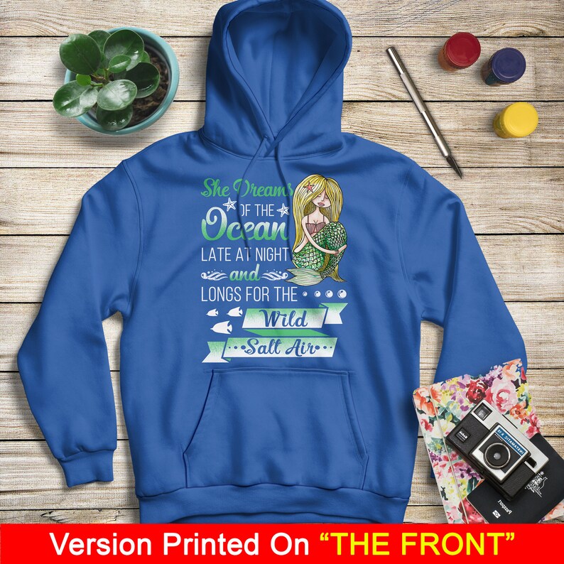 May include: A royal blue hoodie with a mermaid graphic and the text "She Dreams of the Ocean Late at Night and Longs for the... Wild Salt Air..." printed on the front.