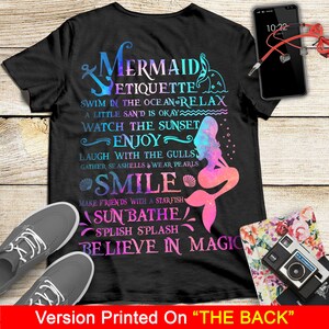 May include: Black t-shirt with a mermaid graphic and text that reads "Mermaid Etiquette: Swim in the ocean & relax, a little sand is okay, watch the sunset, enjoy, laugh with the gulls, gather seashells & wear pearls, smile, make friends with a starfish, sunbathe, splish splash, believe in magic".