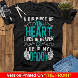 May include: A black t-shirt with a teal blue graphic that says "A big piece of my heart lives in heaven & he is my daddy". The graphic has decorative swirls and wings.