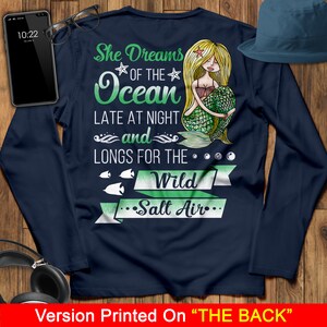 May include: Navy blue long-sleeve shirt with a mermaid illustration and the text "She Dreams of the Ocean Late at Night and Longs for the Wild Salt Air".