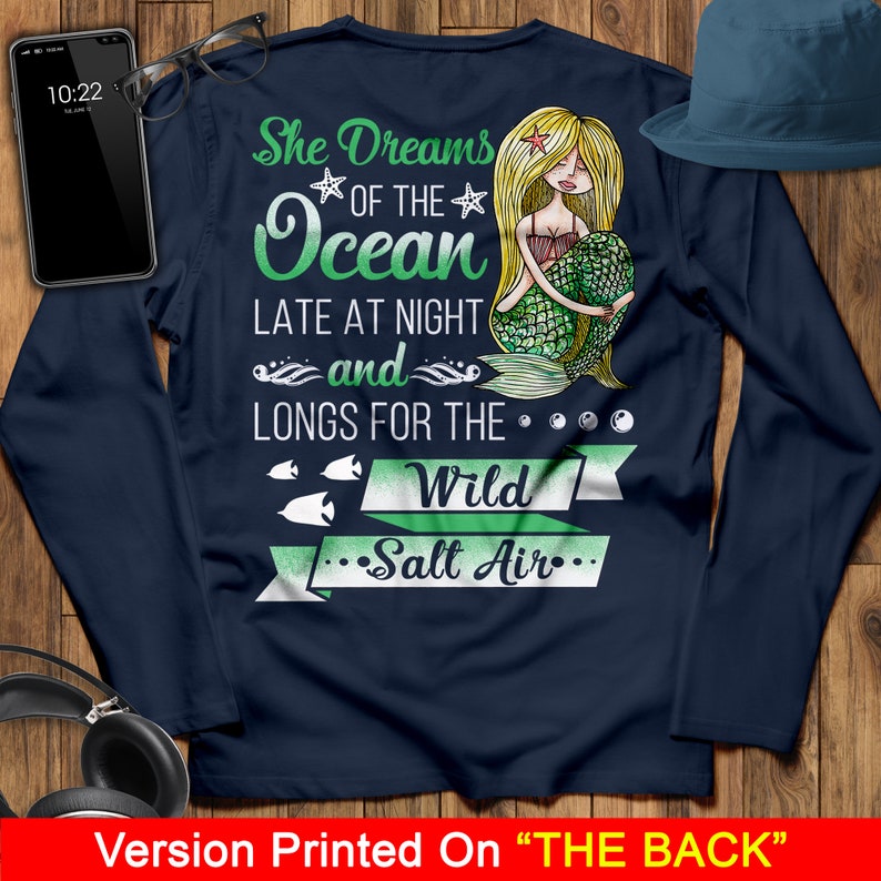 May include: Navy blue long-sleeve shirt with a mermaid illustration and the text "She Dreams of the Ocean Late at Night and Longs for the Wild Salt Air".