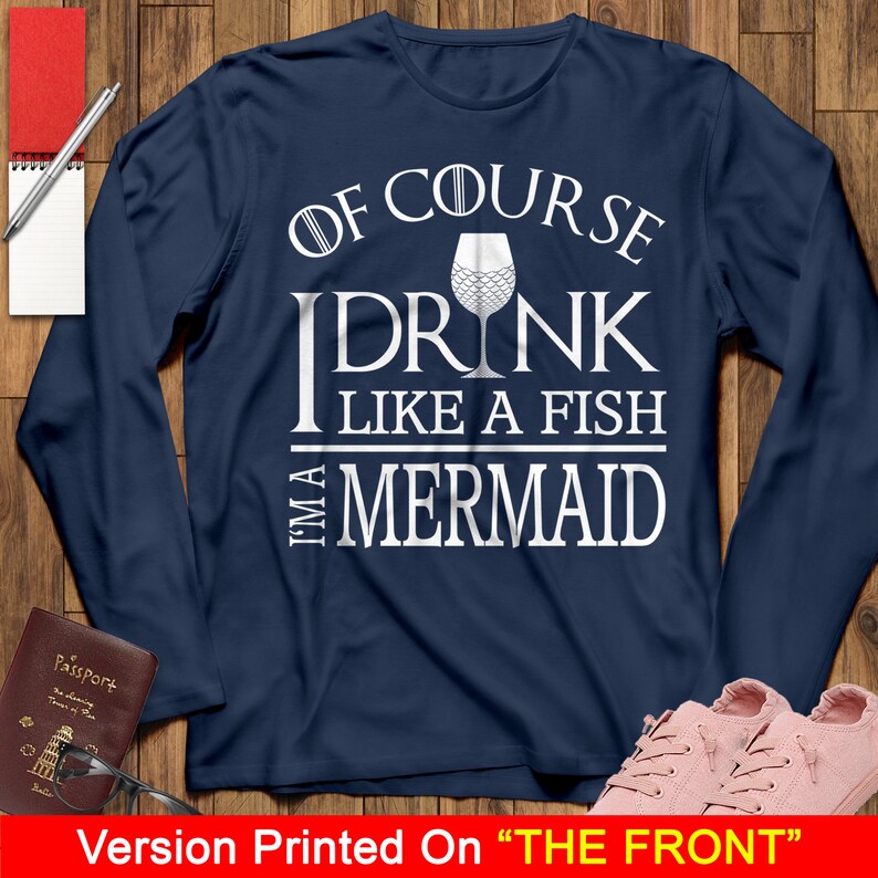 May include: Navy blue long-sleeve shirt with white text that reads "Of course I drink like a fish I'm a mermaid". The text is surrounded by a white circle with a white wine glass with a mermaid tail design inside.
