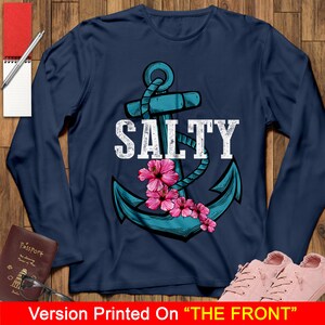 May include: A navy blue long-sleeved t-shirt with a blue anchor and pink flowers. The text "SALTY" is printed in white above the anchor.