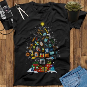 May include: Black t-shirt with a Christmas tree design made up of tools and a light bulb at the top. The tree is surrounded by presents with red, green, and white wrapping paper.