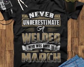 May include: Black t-shirt with gold text that reads "Never underestimate a welder who was born in March".