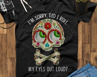 May include: Black t-shirt with a white sugar skull design. The skull has green eyes, red lips, and floral details. The text "I'm sorry, did I roll my eyes out loud?" is printed below the skull.