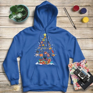 May include: A royal blue hoodie with a Christmas tree design featuring various tools and equipment. The tree is decorated with a star on top and presents at the bottom.