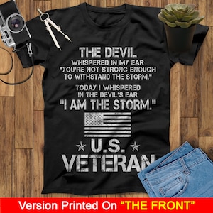 May include: Black t-shirt with a white graphic design featuring a US flag and the text "The Devil whispered in my ear "You're not strong enough to withstand the storm." Today I whispered in the devil's ear "I am the storm."  ★ U.S. ★ VETERAN"