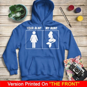 Puede incluir: Una sudadera con capucha azul real con un gr&aacute;fico blanco que dice "Your ain't my aunt" con una figura de palo de una mujer a la izquierda y una sirena a la derecha. El texto "Version Printed On "THE FRONT"" est&aacute; en la parte inferior de la imagen.