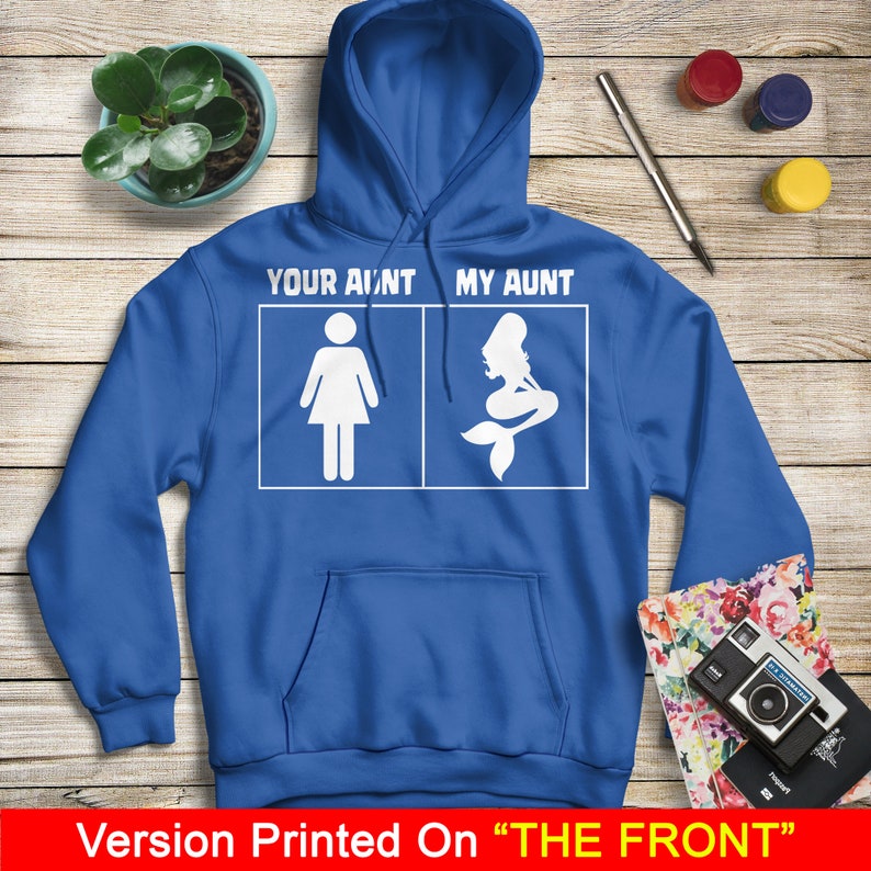 Puede incluir: Una sudadera con capucha azul real con un gr&aacute;fico blanco que dice "Your ain't my aunt" con una figura de palo de una mujer a la izquierda y una sirena a la derecha. El texto "Version Printed On "THE FRONT"" est&aacute; en la parte inferior de la imagen.