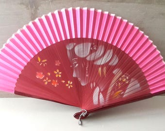 May include: A red and pink hand fan with a white floral design and a woman's face painted on it.