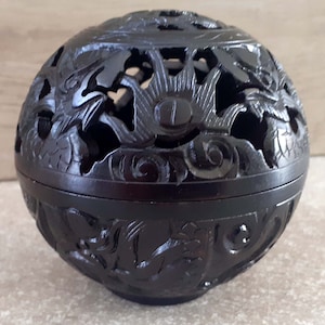 May include: A dark brown, spherical decorative box with intricate carved dragon and floral designs. The box is made of wood and has a lid that fits snugly on the base. The carvings are detailed and create an openwork effect.