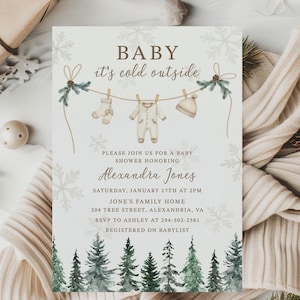 May include: Baby shower invitation with the text "BABY it's cold outside." The invitation features illustrations of baby clothes hanging on a clothesline, snowflakes, and a forest scene. The invitation is for Alexandra Jones.