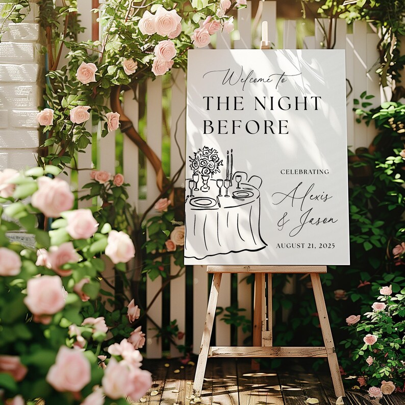 May include: A white sign on a wooden easel with the text "Welcome to The Night Before" and the names Alexis & Jason, celebrating August 21, 2025. The sign is surrounded by pink roses and greenery.