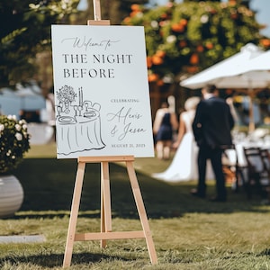 May include: A white sign on a wooden easel with the text "Welcome to THE NIGHT BEFORE" and "Celebrating Alexis & Jason August 21, 2025". A sketch of a table setting is also on the sign. The sign is outdoors.