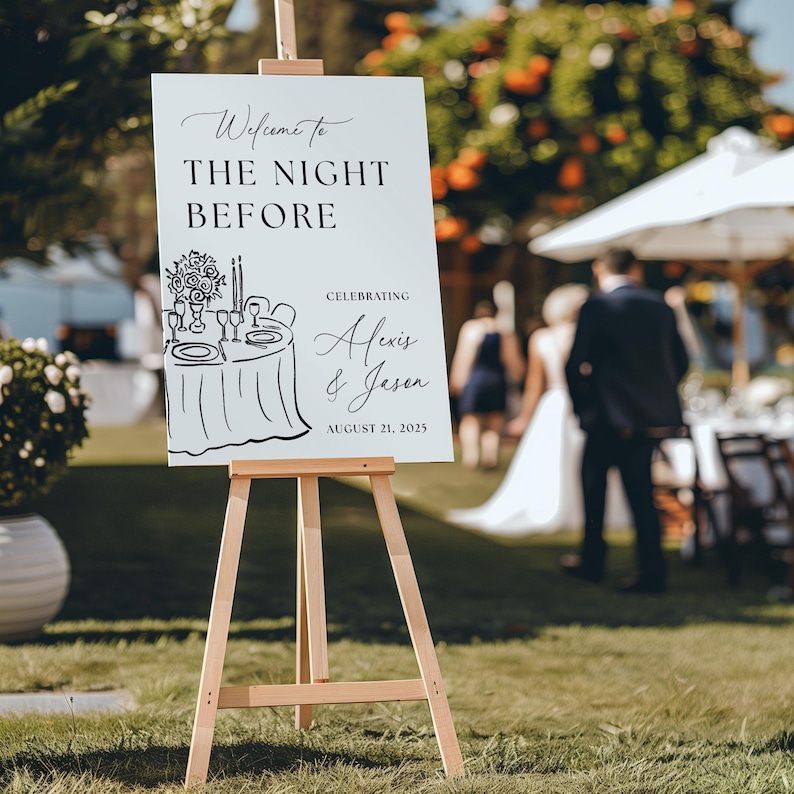May include: A white sign on a wooden easel with the text "Welcome to THE NIGHT BEFORE" and "Celebrating Alexis & Jason August 21, 2025". A sketch of a table setting is also on the sign. The sign is outdoors.