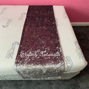 May include: A plush, crushed velvet bed runner in a deep purple colour with a silver sheen. The runner has the text "Stylish Interiors" embroidered in white on the fabric.