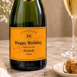 May include: A dark green glass champagne bottle with a custom orange label featuring the text CHAMPAGNE, 30, Happy Birthday, MARCH 26, 1992, ELIJAH, and CHEERS!. The label includes a crown icon and 750 ml and 12% alc/vol volume and alcohol content.