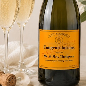 Peut inclure: Une bouteille de champagne avec un col en aluminium doré et une étiquette orange personnalisée indiquant Just Married, Congratulations, 03.03.23, Mr. & Mrs. Thompson, et Cheers to your happily ever after, avec 750 ml et 12% d'alcool indiqués.